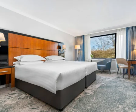 Elegant hotel room with double bed, stylish decor, and a view of greenery through the window.