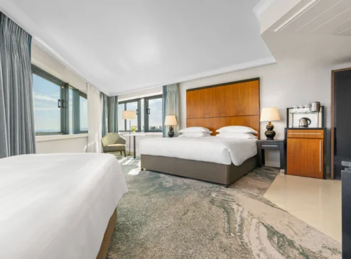 Bright hotel room with sea view, double bed, and seating area. Modern and inviting space.