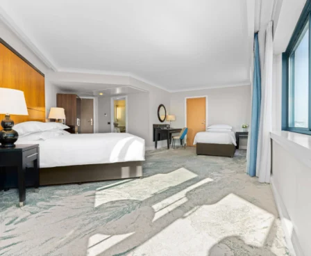 Spacious hotel room with large windows, a double and a single bed, and cosy lighting.
