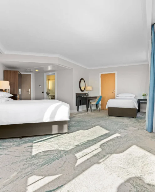 Spacious hotel room with large windows, a double and a single bed, and cosy lighting.