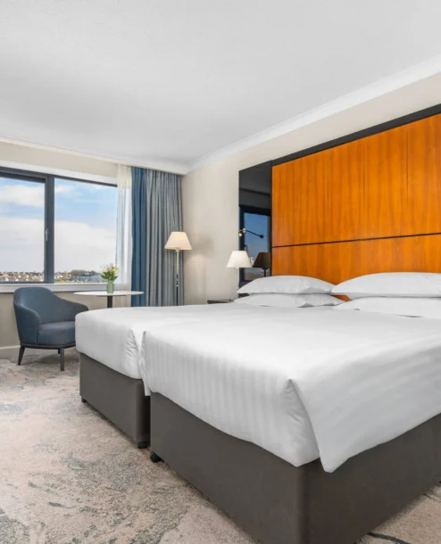 Elegant hotel room with twin beds, a city view, and stylish modern decor.