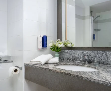 Modern hotel bathroom with fresh towels and flowers on granite counter.