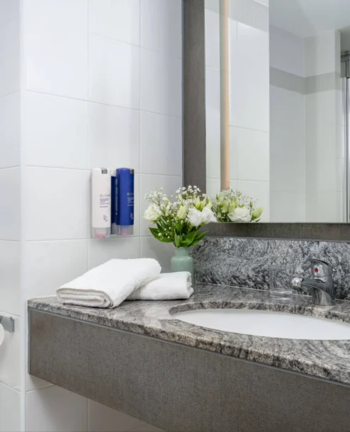 Modern hotel bathroom with fresh towels and flowers on granite counter.