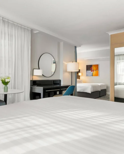 Modern hotel room with double beds, cosy seating area, and warm ambient lighting.