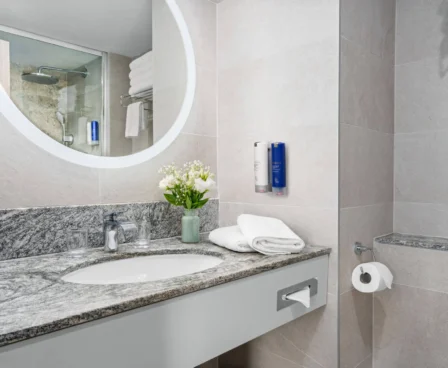 Elegant hotel bathroom with marble countertop, fresh flowers, and plush towels.