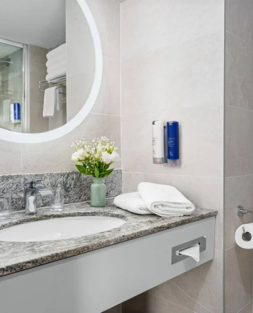 Elegant hotel bathroom with marble countertop, fresh flowers, and plush towels.