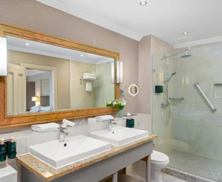 Elegant hotel bathroom with twin sinks, large mirror, and spacious glass shower.