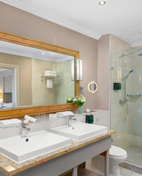 Elegant hotel bathroom with twin sinks, large mirror, and spacious glass shower.