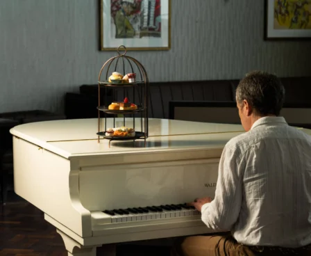 Gentleman playing piano in elegant hotel lounge with afternoon tea stand.