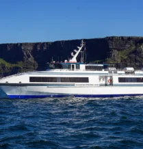 A family enjoys a scenic ferry ride near dramatic Irish cliffs under a clear blue sky.