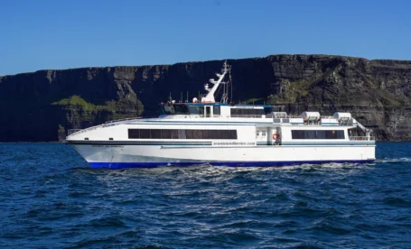 A family enjoys a scenic ferry ride near dramatic Irish cliffs under a clear blue sky.