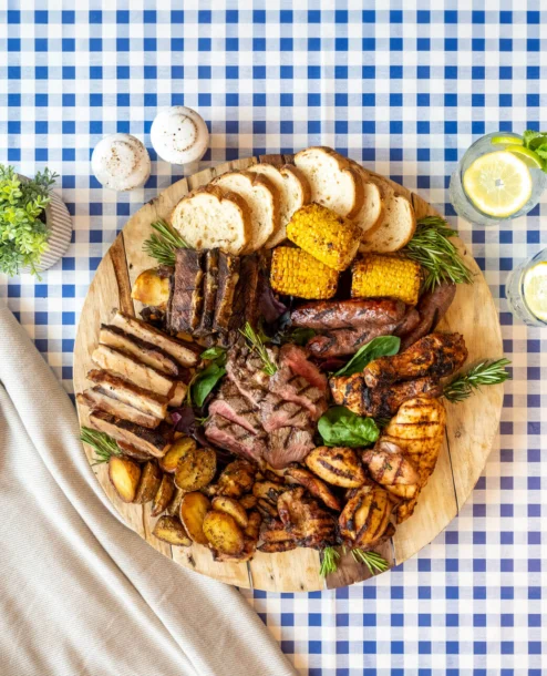 Family enjoying diverse platter in a cosy picnic setting with drinks and camera.