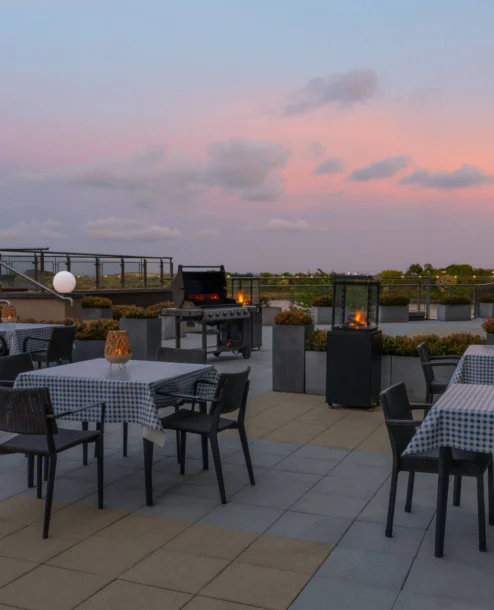 Rooftop dining area at sunset with tables, chairs, and ambient lighting.