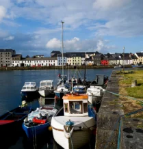 Colourful boats docked along a scenic Galway harbour under a bright sky.