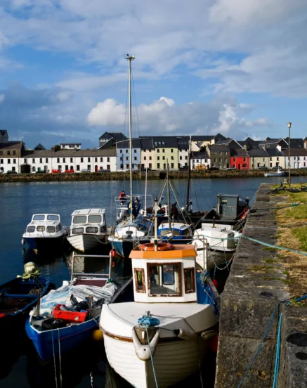 Colourful boats docked along a scenic Galway harbour under a bright sky.