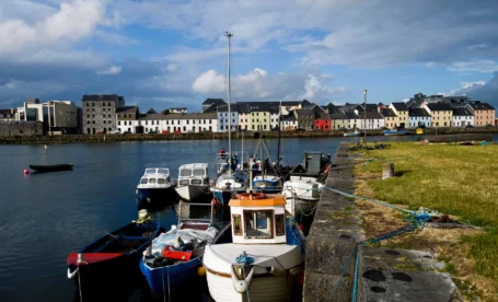 Colourful boats docked along a scenic Galway harbour under a bright sky.