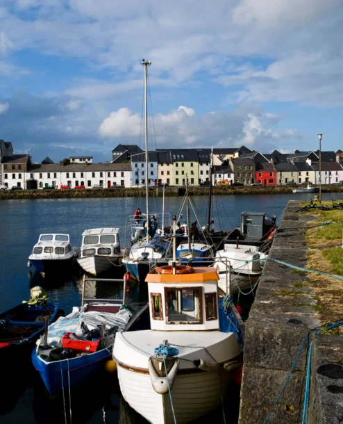 Colourful boats docked along a scenic Galway harbour under a bright sky.
