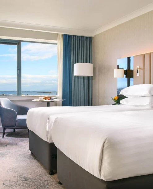 Elegant hotel room with sea view, twin beds, and a cosy seating area.