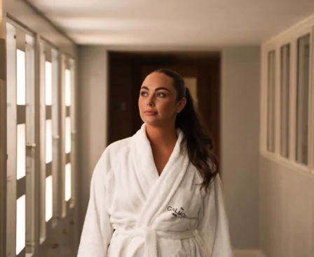 Woman in a white robe walks through The Galmont Hotel spa corridor.
