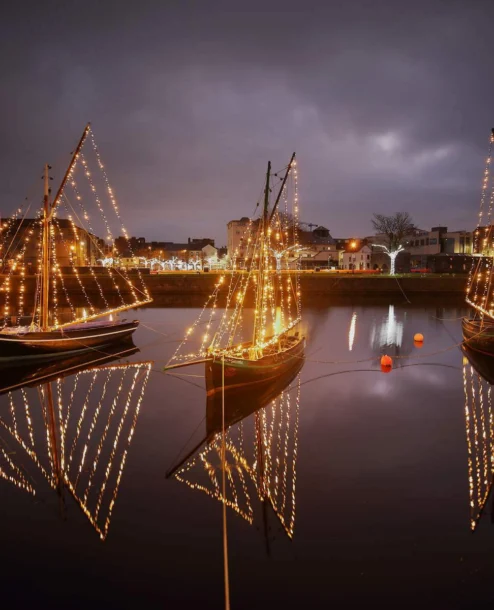 Illuminated boats reflecting on calm evening waters near The Galmont Hotel & Spa.