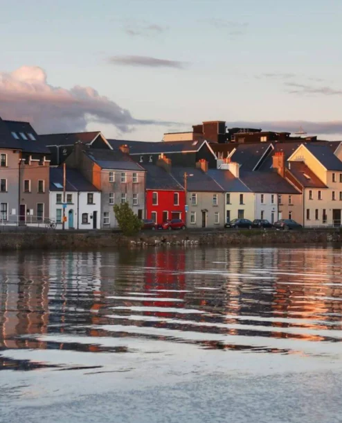 Colourful waterfront townhouses reflecting in calm evening waters.