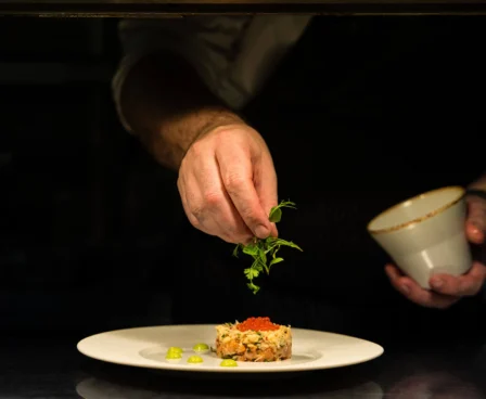 Chef garnishing gourmet dish in elegant hotel dining setting.