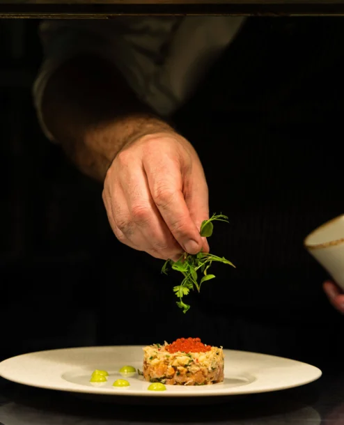 Chef garnishing gourmet dish in elegant hotel dining setting.