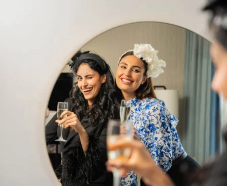 Two women smiling, holding champagne glasses in a hotel room.