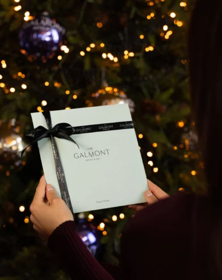 Woman holding Galmont Hotel & Spa gift voucher by a decorated Christmas tree.