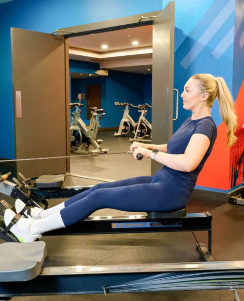 Woman enjoying workout on rowing machine in vibrant hotel gym with modern equipment.