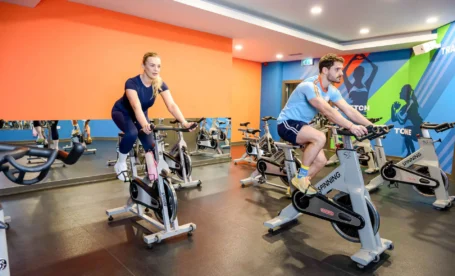 Couple enjoying workout on stationary bikes in a vibrant hotel gym.