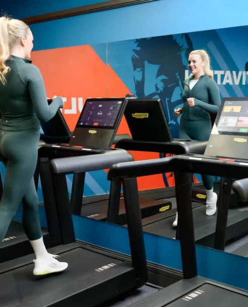 Woman jogging on treadmill in hotel gym with vibrant wall art.