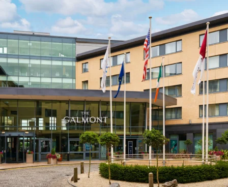The Galmont Hotel entrance with flags and modern glass façade on a sunny day.