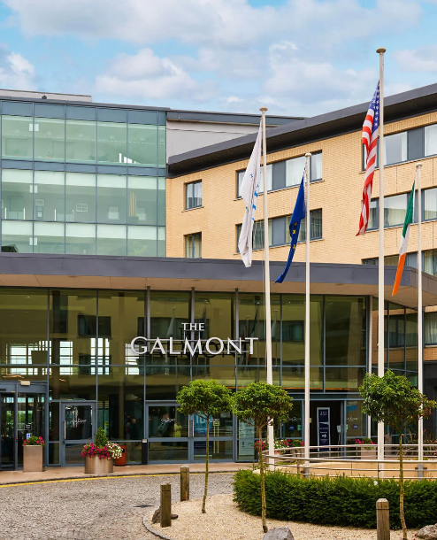 The Galmont Hotel entrance with flags and modern glass façade on a sunny day.