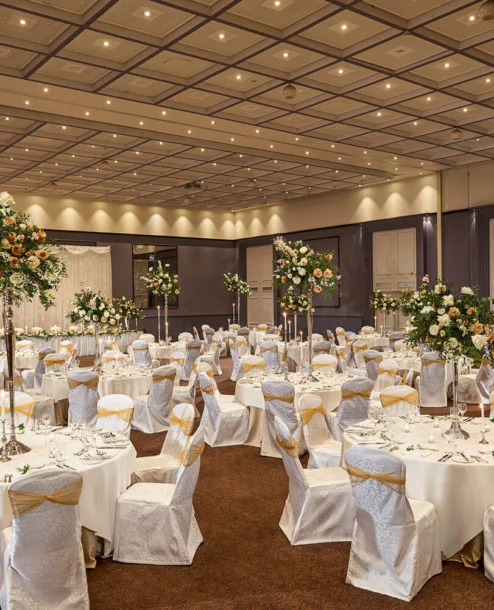 Elegant banquet hall set for a wedding with white tablecloths and floral centrepieces.