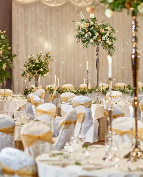 Elegant banquet hall with white and gold decor, floral centrepieces, and ambient lighting.