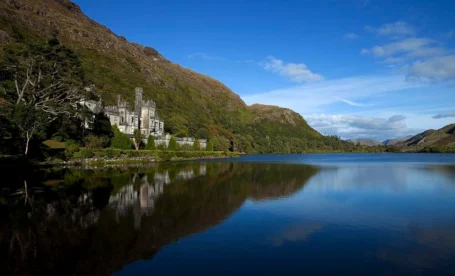Majestic lakeside hotel surrounded by mountains under a clear blue sky.
