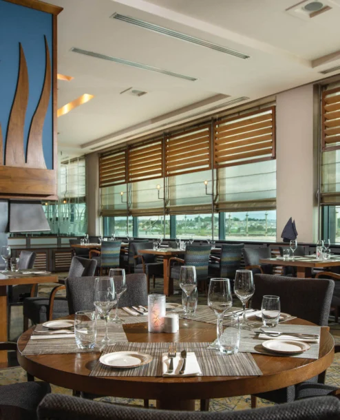Elegant hotel restaurant with set tables by large windows offering a scenic view.