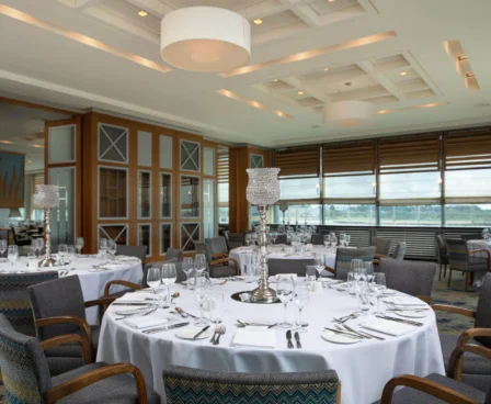 Elegant dining room with round tables, set for a family gathering, large windows overlooking water.
