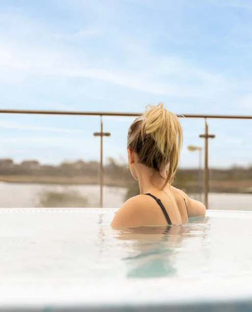 Woman relaxing in outdoor hotel hot tub overlooking serene lake view.