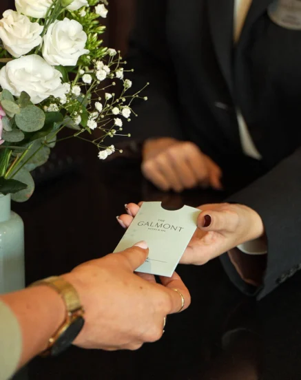 Warm hotel welcome at The Galmont, guest receiving room key by floral arrangement.