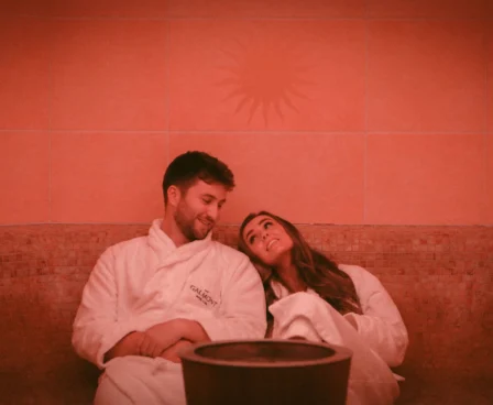 A couple relaxes in cosy robes at The Galmont Hotel & Spa sauna, with warm amber lighting.