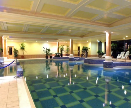 Luxurious indoor pool at The Galmont Hotel & Spa, surrounded by pillars and lush plants.