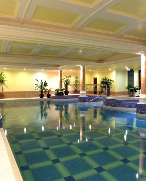 Luxurious indoor pool at The Galmont Hotel & Spa, surrounded by pillars and lush plants.