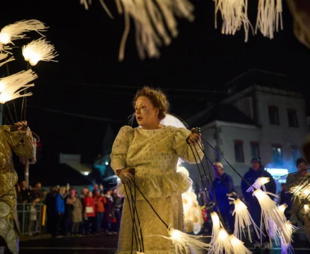 Festive performers in costumes carrying illuminated decorations at night near The Galmont Hotel.