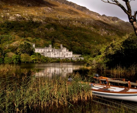 Elegant hotel by serene lake with mountains; a boat and lush greenery in the foreground.