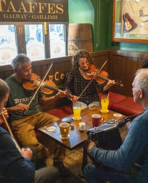 Group enjoying traditional music session at cosy Irish pub with drinks on the table.