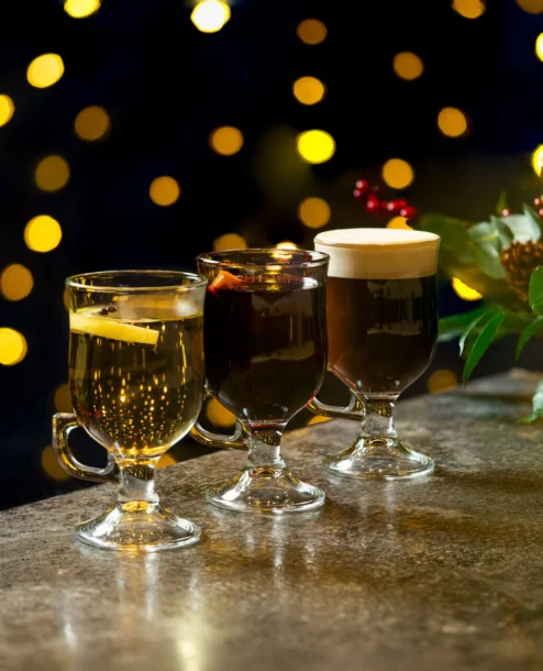 Three festive drinks on a table with soft bokeh lights in a cosy, inviting hotel setting.