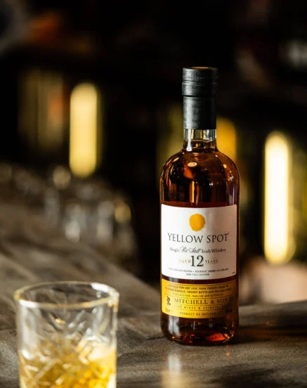 A bottle of Yellow Spot 12 Year Old Irish whiskey on a bar with a glass of whiskey nearby.