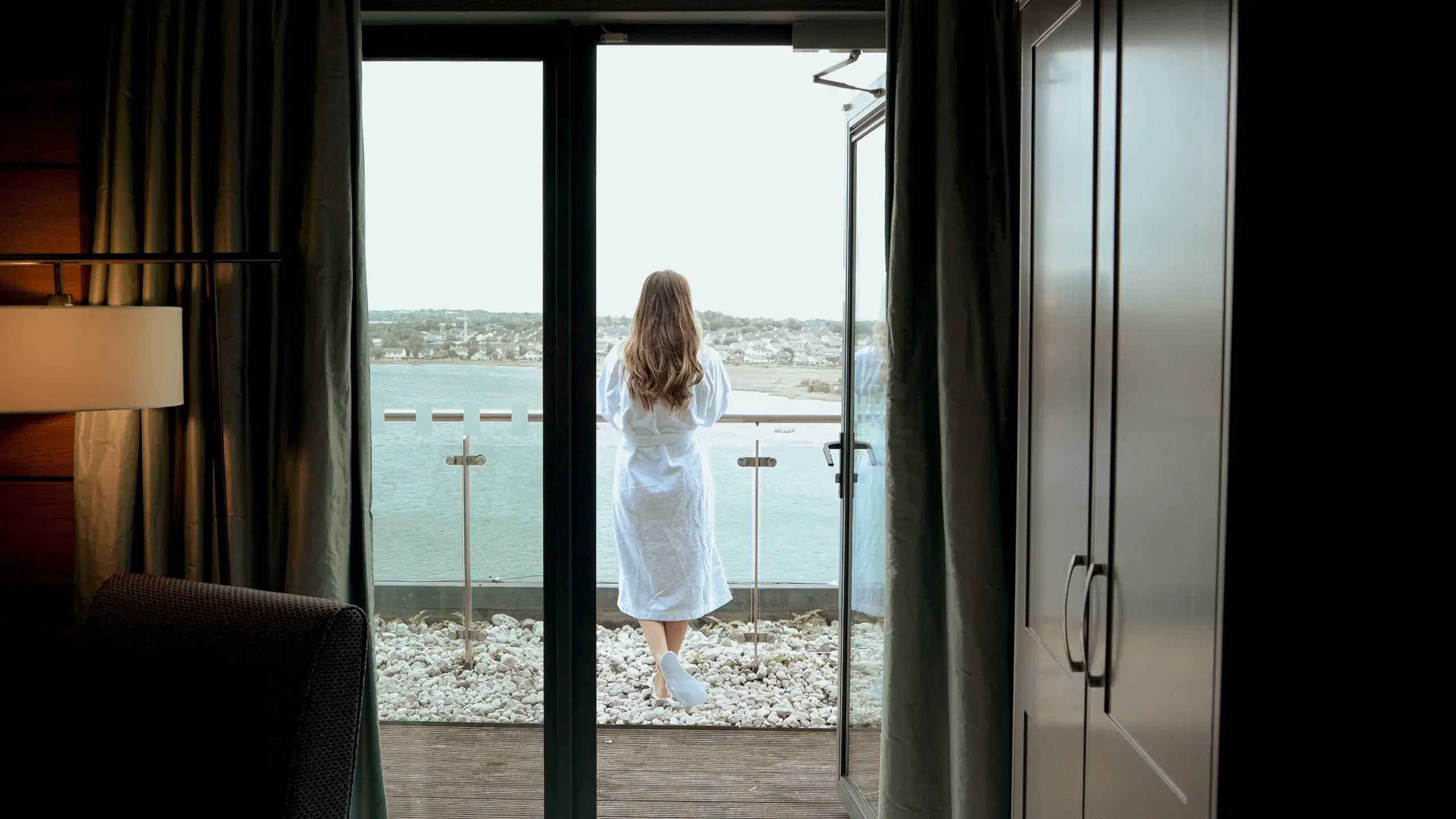 Woman in robe enjoying sea view from hotel balcony.